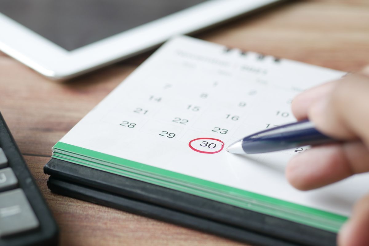 A hand marking a date on a calendar with a pen, representing booking and scheduling coordination