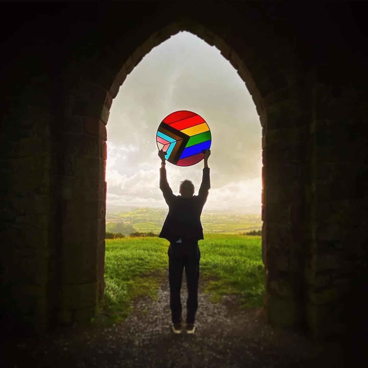 A stained glass panel held aloft through a stone gothic arch in west Wales, with rolling green Welsh countryside stretching beyond — One Day Beginners Stained Glass Course Llandeilo West Wales with Simon Howard